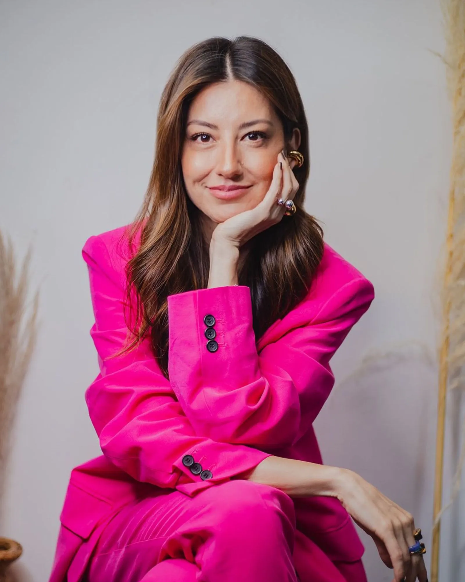 Mujer con traje fucsia sonriente apoyando su rostro en la mano